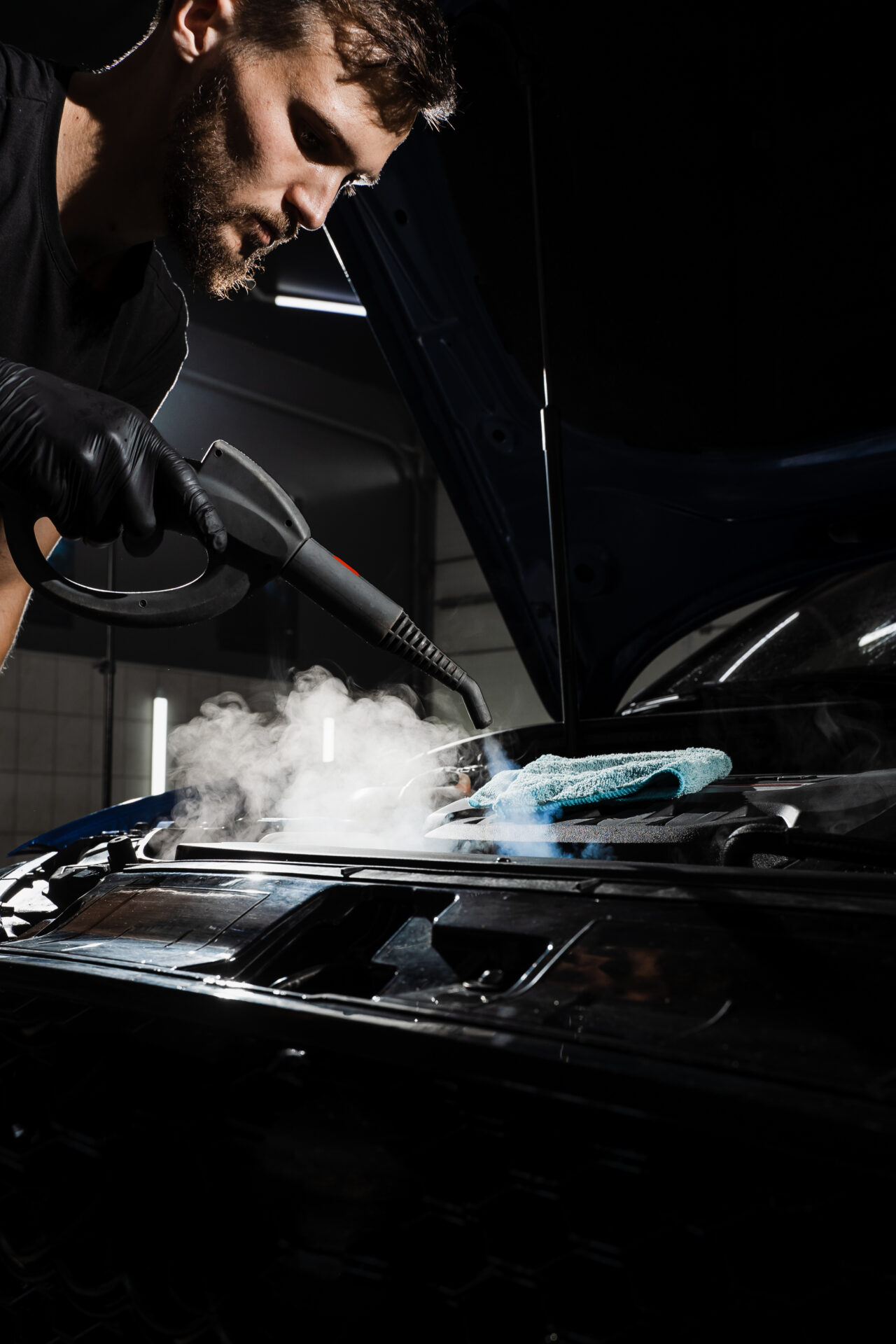 Process of steam cleaning car engine from dust and dirt. Steaming washing of motor of auto in detailing auto service.